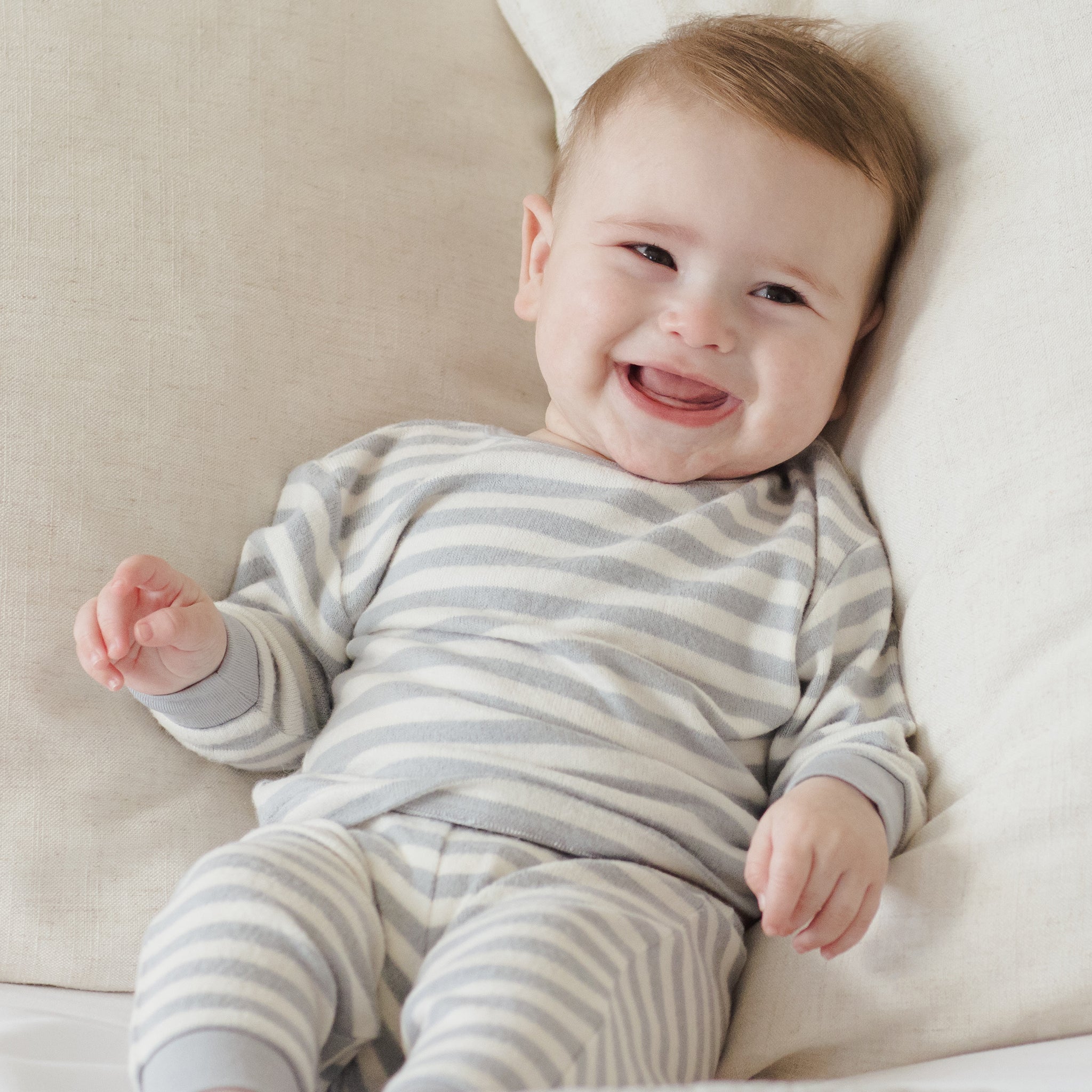 Baby wearing a gray and white striped onesie lying on a beige couch.