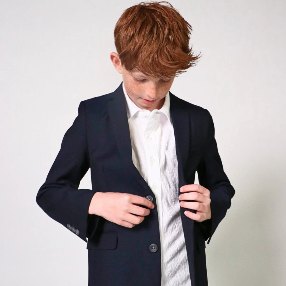 Person wearing a navy blazer over a white shirt with a light-colored background