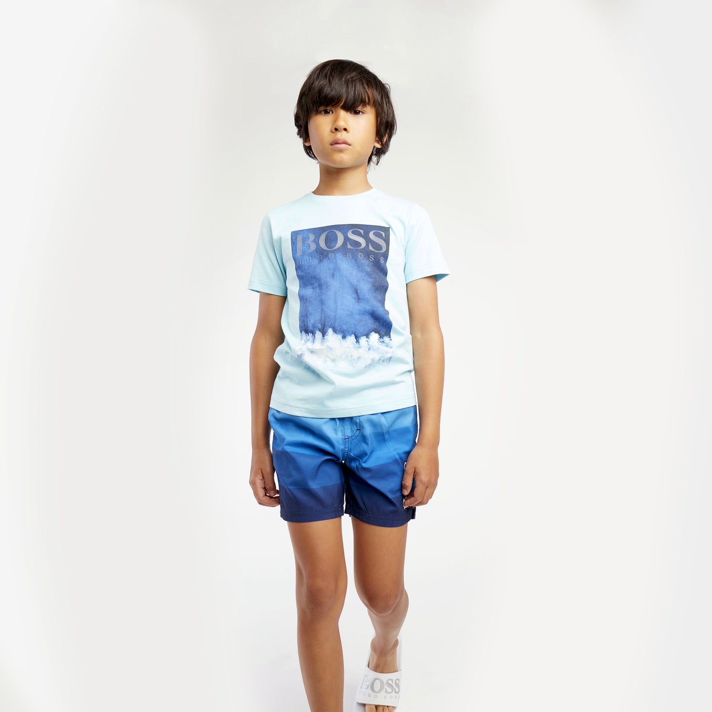 Boys wearing Graphic BOSS short sleeve t-Shirt. Silver BOSS logo on image . Light blue t-shirt with shaded blues in graphic. Slim Fit. 100% cotton